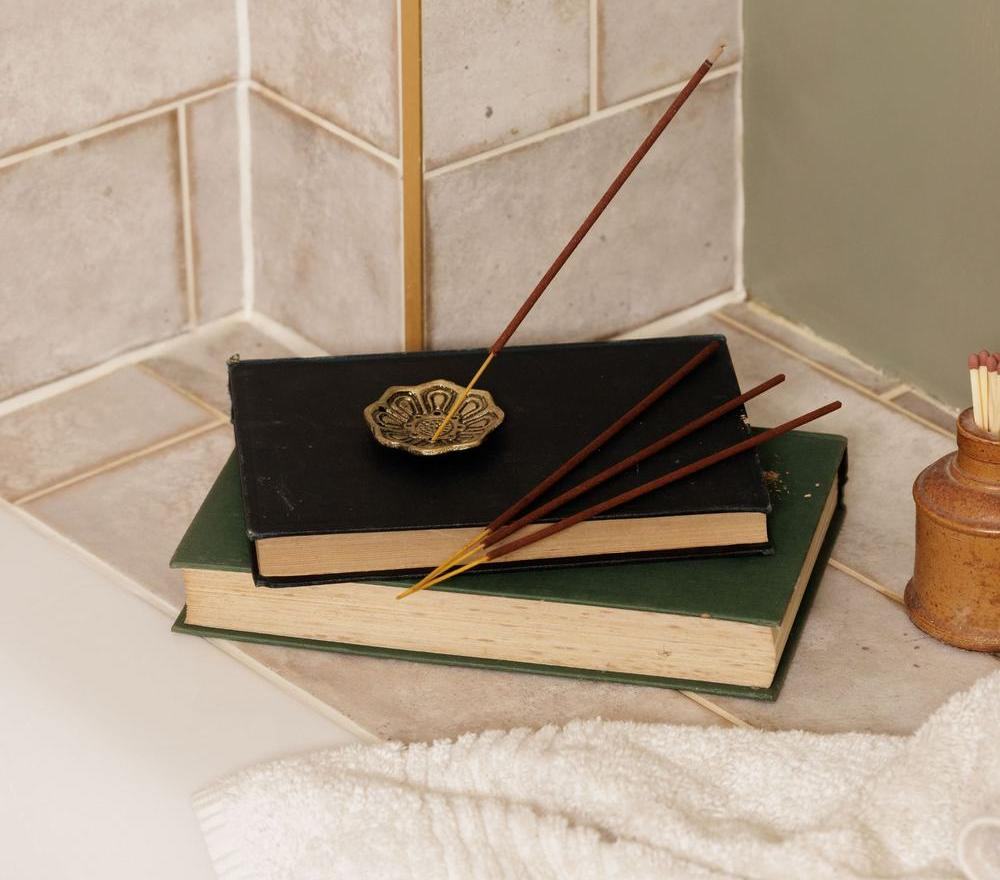Incense sticks in a holder on a stack of books on a bathroom shelf.