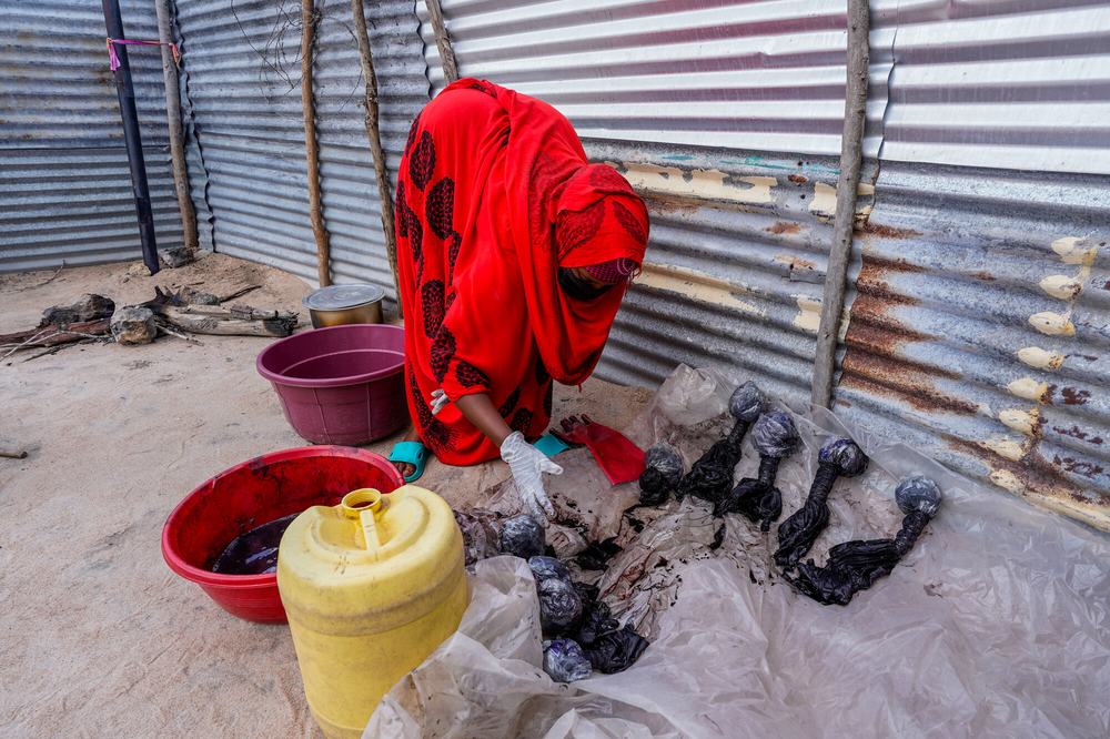 a woman, surrounded by several containers of dye, leans over freshly dyed garments laid out on a plastic sheet.
