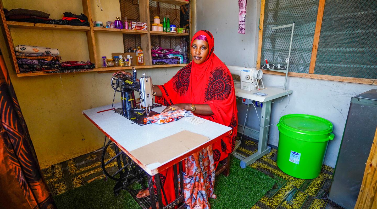 a woman sat at a sewing machine, stitching a colourful patterned garment.