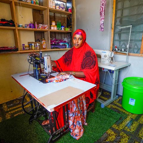 a woman sat at a sewing machine, stitching a colourful patterned garment.