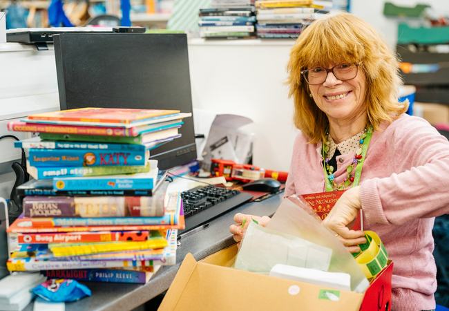 Volunteer Harriet pricing up childrens books at Oxfam Shop Magdalen Street, Norwich