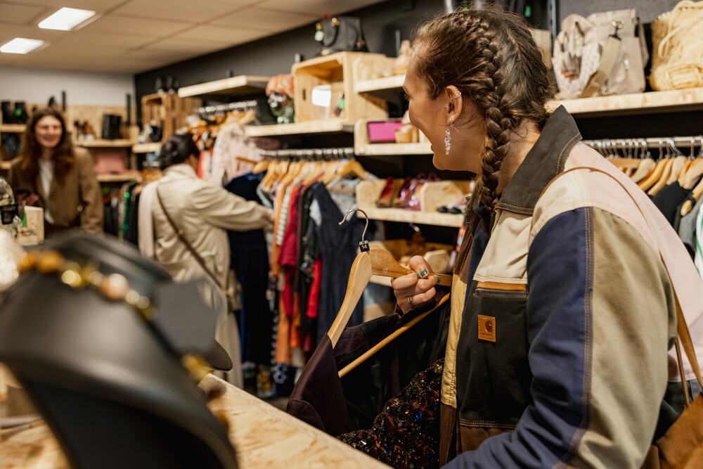 Lady smiles to another shopper while holding clothing