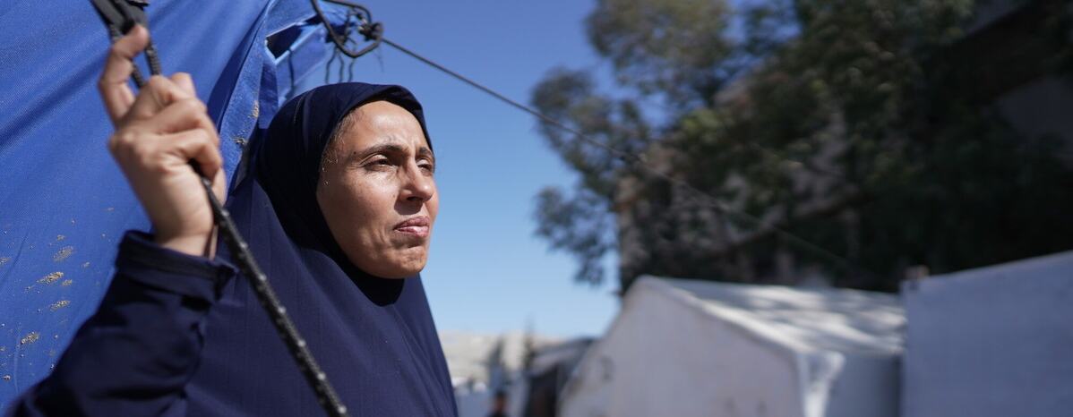 A woman standing outside a blue tent looking out to the distance in the Occupied Territory of Palestine