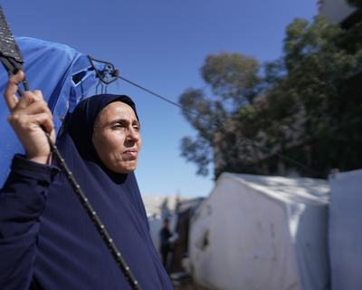A woman standing outside a blue tent looking out to the distance in the Occupied Territory of Palestine