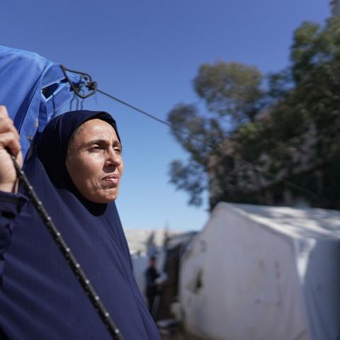 A woman standing outside a blue tent looking out to the distance in the Occupied Territory of Palestine