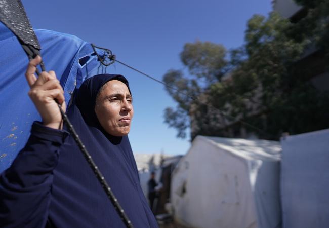 A woman standing outside a blue tent looking out to the distance in the Occupied Territory of Palestine