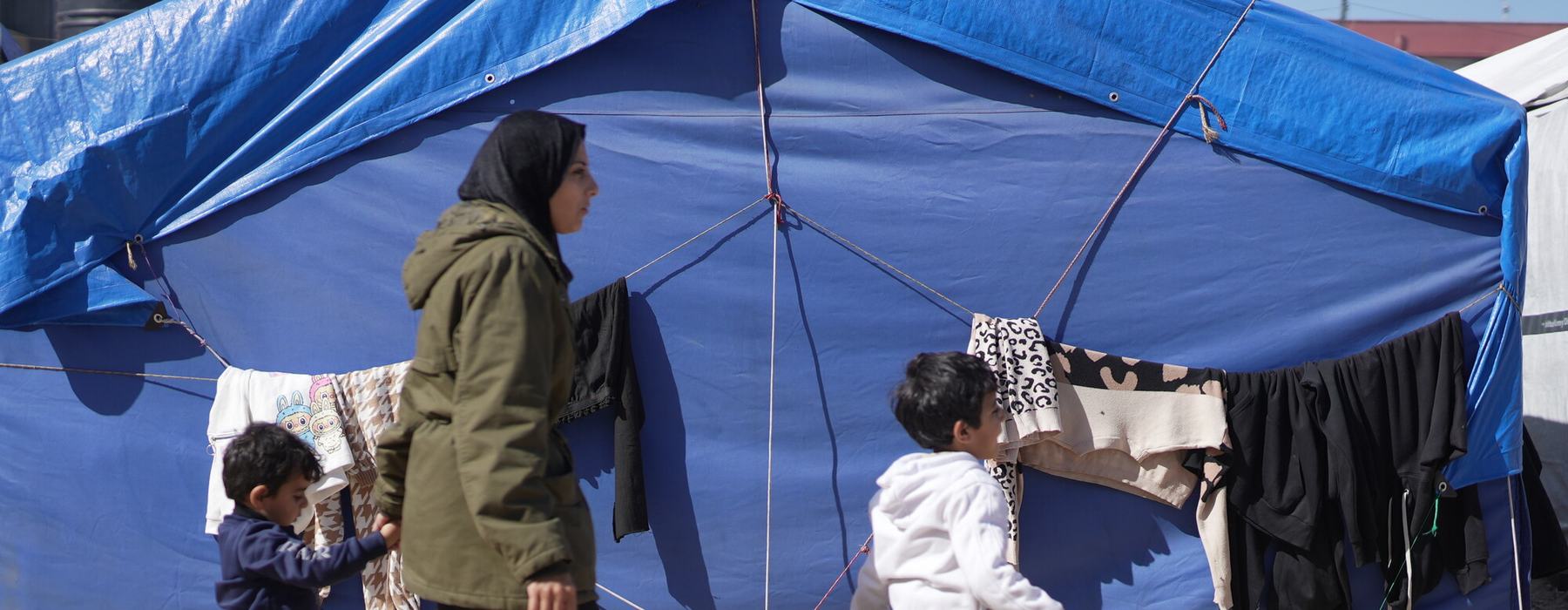 Rania walks with two of her sons in front of her blue tent in a makeshift tent camp in Gaza City