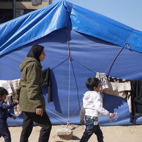 Rania walks with two of her sons in front of her blue tent in a makeshift tent camp in Gaza City