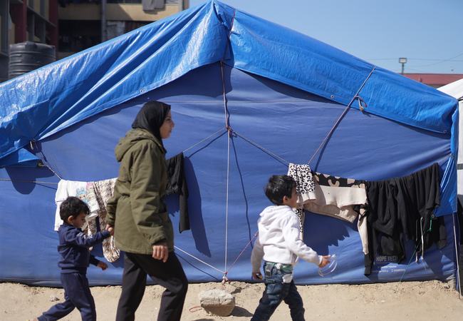 Rania walks with two of her sons in front of her blue tent in a makeshift tent camp in Gaza City