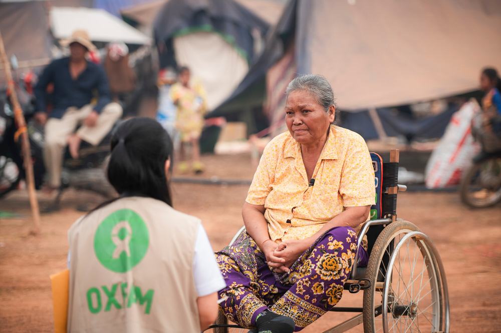 A woman in an Oxfam-branded vest speaks to a woman in a wheelchair in Chong Kal camp, Cambodia.