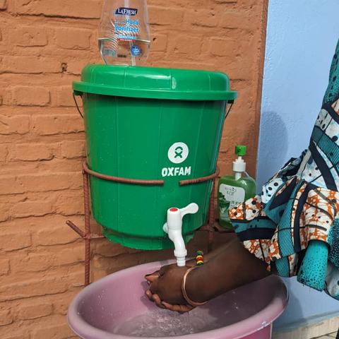 A person washing their hands at an Oxfam bucket handwashing stand.
