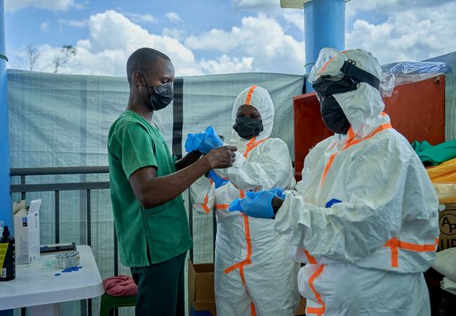 Joseph Kandule assisting team in protective suits with gloves.