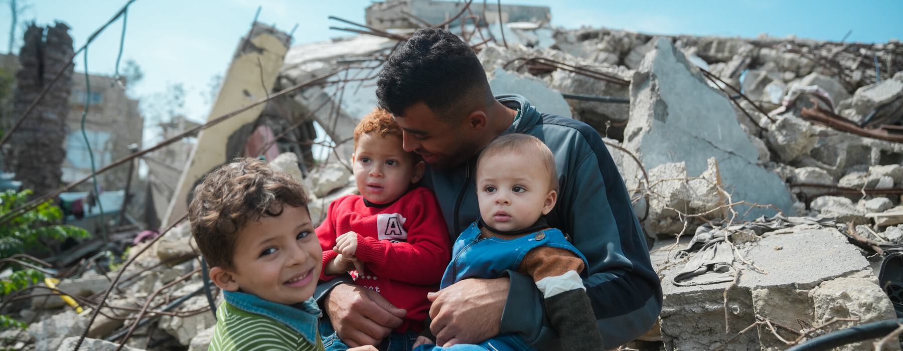Mohammed sitting atop the rubble of his house with his three children.