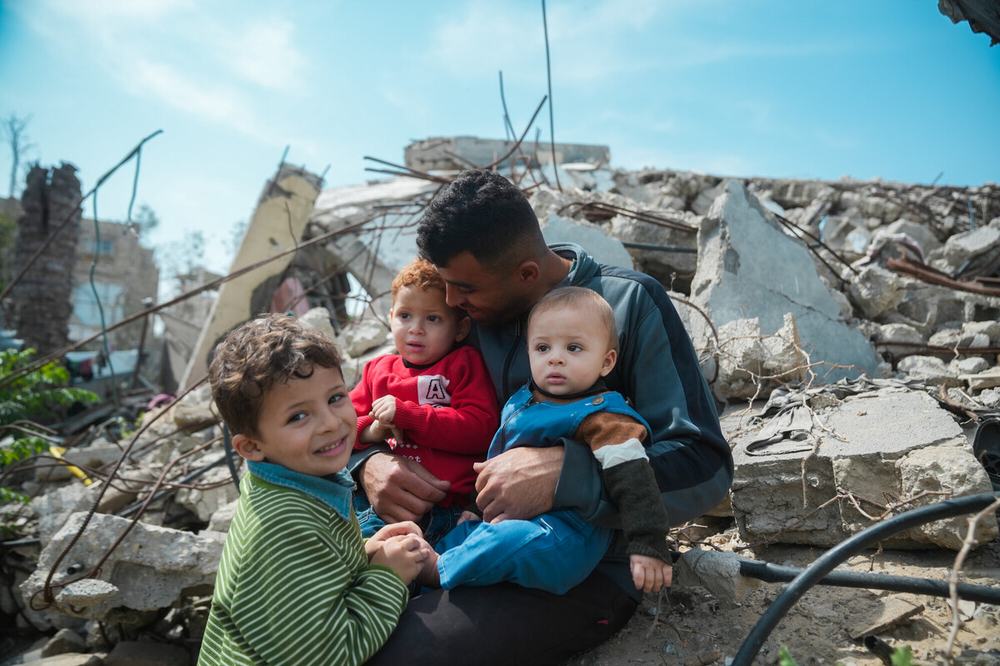 A man sitting on top the rubble of his house with his three children.