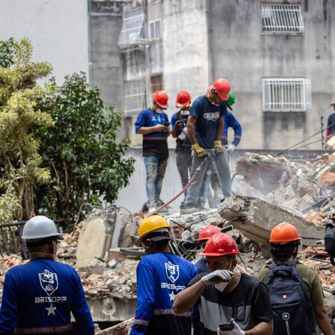 Rescue teams are searching for victims in the San Bernardino area of Caracas. Men in hard hats stand on top of rubble with equipment.
