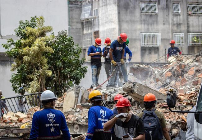 Rescue teams are searching for victims in the San Bernardino area of Caracas. Men in hard hats stand on top of rubble with equipment.