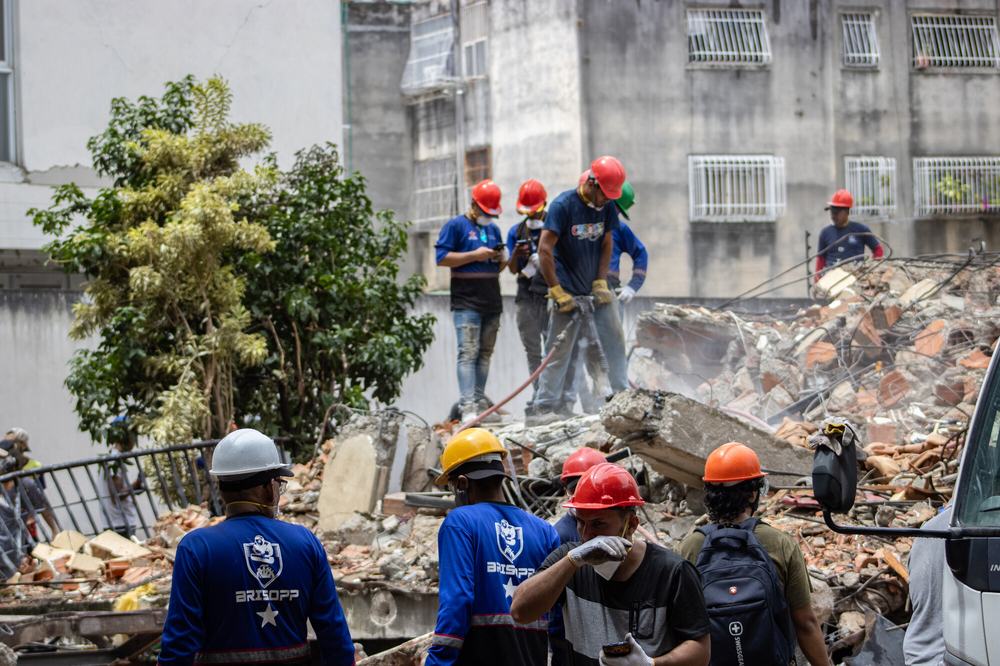Rescue teams are searching for victims in the San Bernardino area of Caracas. Men in hard hats stand on top of rubble with equipment.