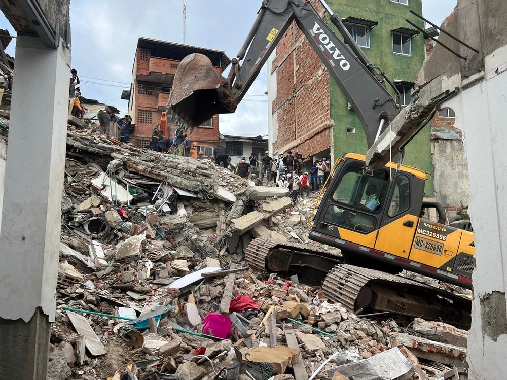 Emergency response teams and heavy machinery conduct search and debris removal operations among the rubble of buildings damaged by the earthquake. The image shows part of the response efforts in an urban area of the municipality.
