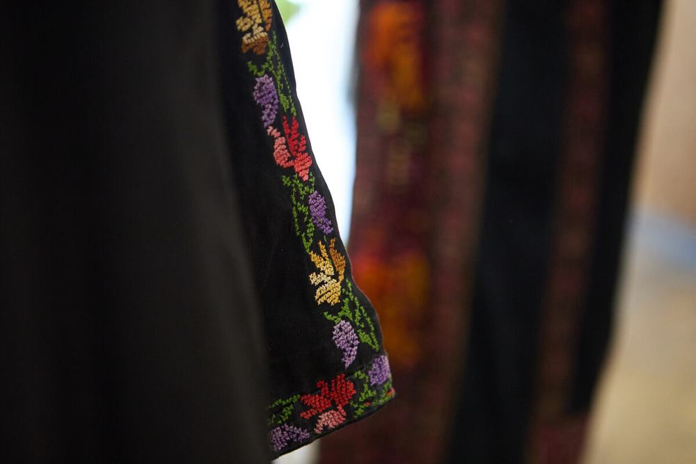 A close up of the sleeve of a black thobe to demonstrate the detail in the stitching of red, gold and purple flowers with green leaves.