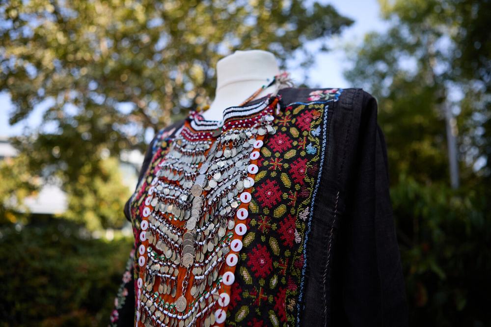 A black dress from Palestine with traditional tatreez embroidery depicting large red flowers and smaller flowers in blue and white.