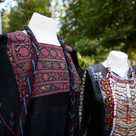 Two traditional Palestinian dresses (thobes) in black fabric with traditional embroidery (tatreez) in pink, blue, yellow and orange threads.