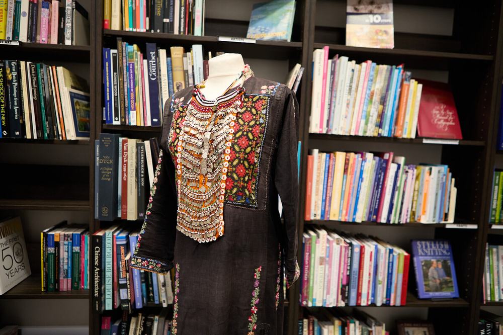 A black thobe thought to have been made in the 1960s-70s with bold red and green embroidery and shiny white and silver buttons embellishing the design.
