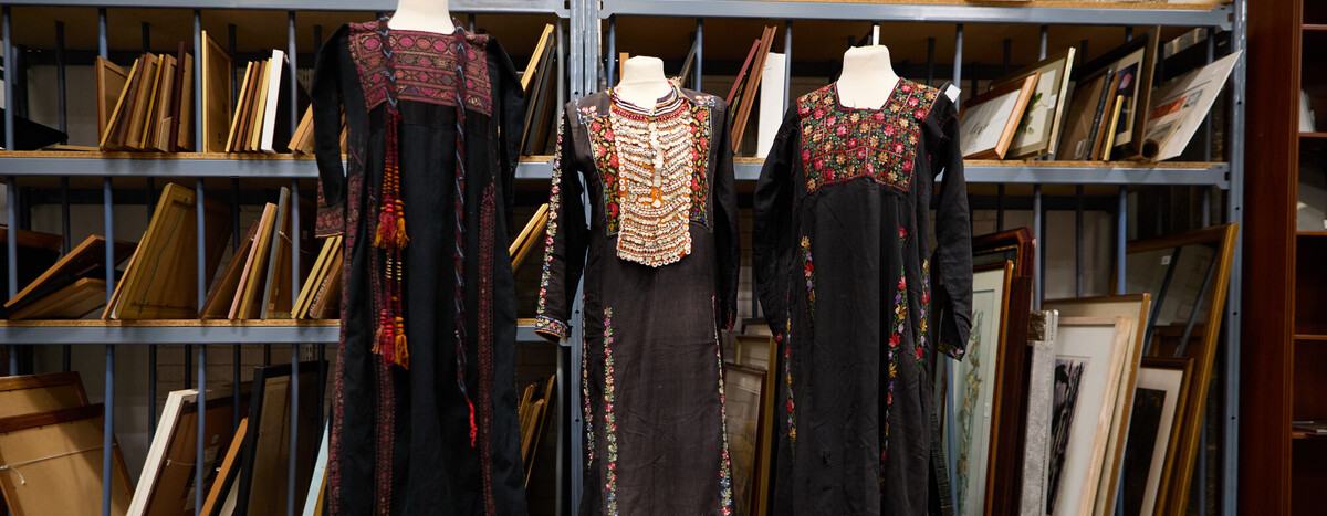 Three traditional Palestinian dresses in black fabric that feature brightly coloured tatreez (embroidery) in intricate designs on the upper part of the dresses.