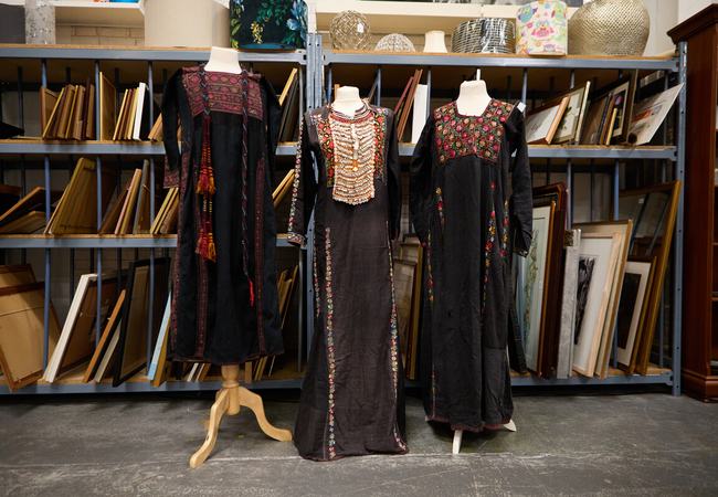 Three traditional Palestinian dresses in black fabric that feature brightly coloured tatreez (embroidery) in intricate designs on the upper part of the dresses.