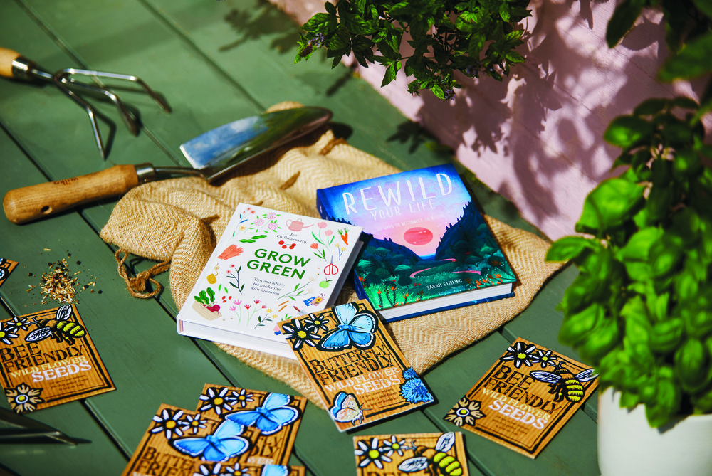 Packets of seeds for butterflies and two books on gardening with gardening equipment nearby outside