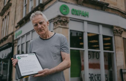 Phil holding up one of his Oxfam press releases in front of his local Oxfam shop.