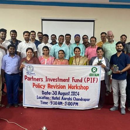 A group of men and women in a hotel function room in Chandrapur, Nepal standing around a white banner promoting the Partners Investment Fund and the Policy Revision Workshop on 30 August 2024.