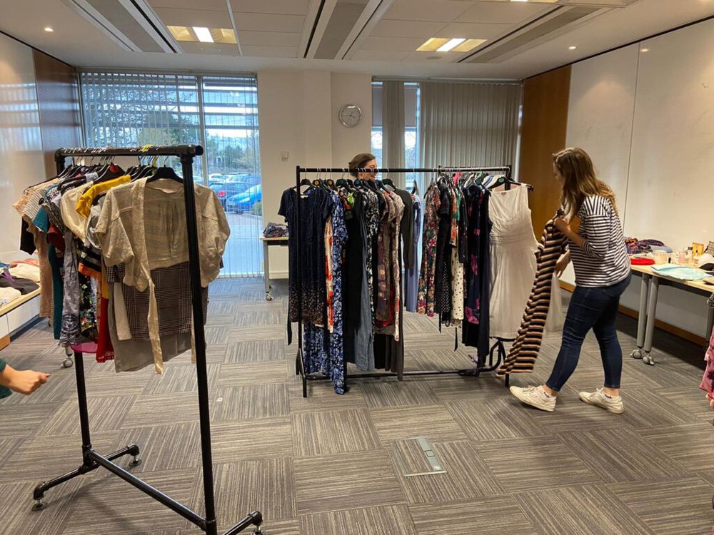 A women in a striped top stands looking at a row of second-hand clothes in a workplace swap shop