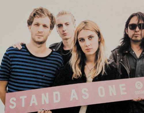 Four people holding a sign reading "Stand as One"