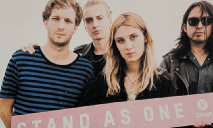 Four people holding a sign reading "Stand as One"
