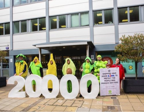 A group of campaigners dresses as fruit holding a bit number '20000' and a placard reading "Shoppers have asked Lidl to protect the people who produce our food".