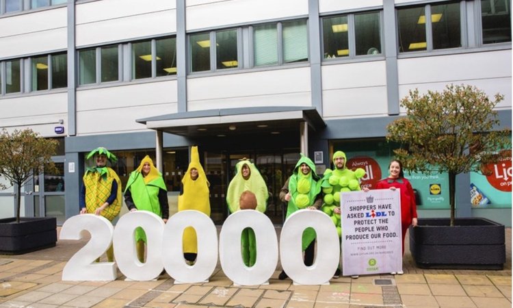 A group of campaigners dresses as fruit holding a bit number '20000' and a placard reading "Shoppers have asked Lidl to protect the people who produce our food".