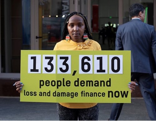Climate activist Elizabeth Wathuti holds a sign reading '133,610 people demand loss and damage finance now'.