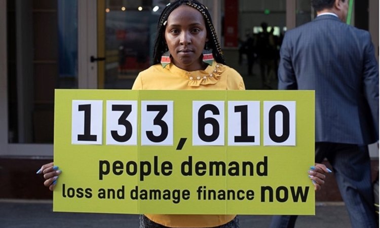 Climate activist Elizabeth Wathuti holds a sign reading '133,610 people demand loss and damage finance now'.