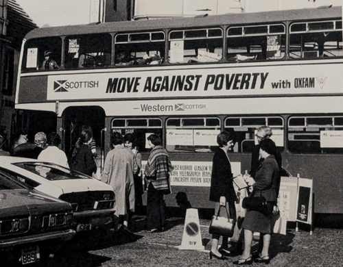 A black and white photo of a double decker bus with a poster for Oxfam's 'Move Against Poverty' campaign on the side.