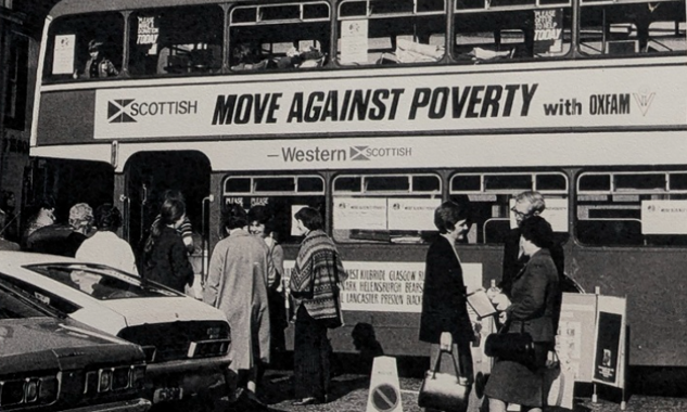 A black and white photo of a double decker bus with a poster for Oxfam's 'Move Against Poverty' campaign on the side.