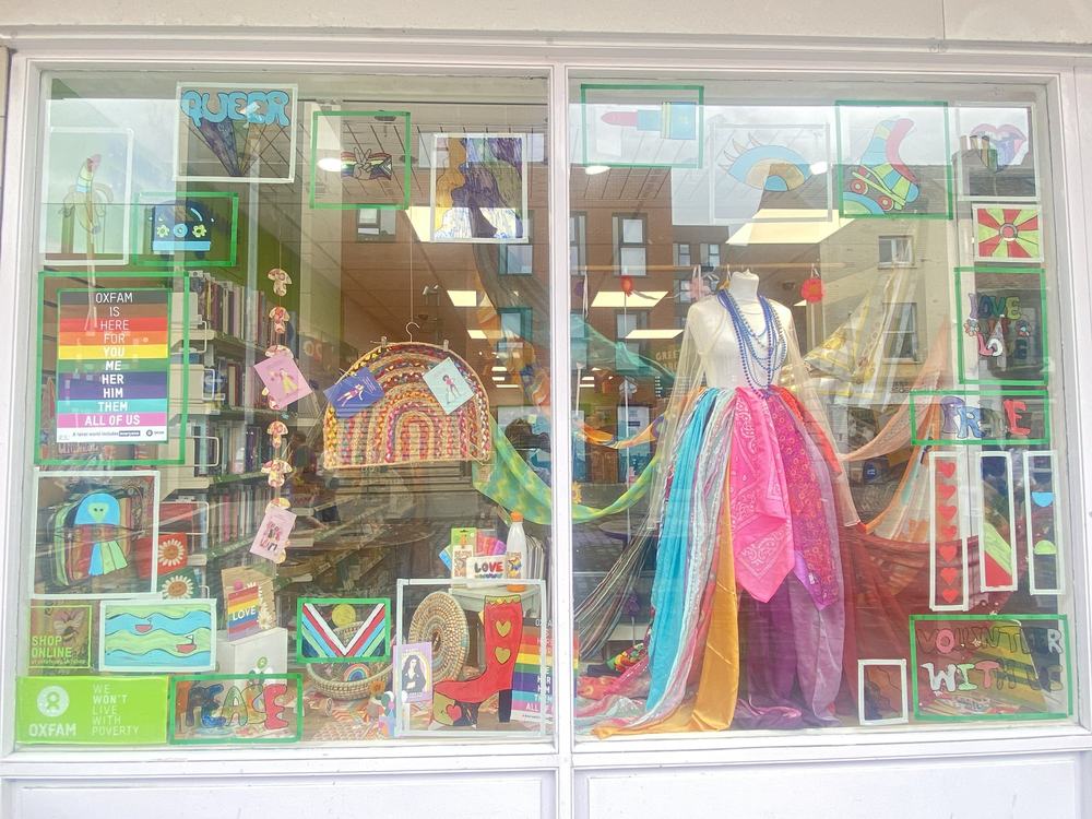 Oxfam shop window in Lincoln brightly decorated with rainbow colours and items relating to Pride and LGBTQIA+ available to buy.