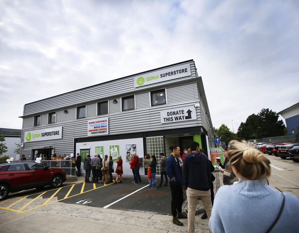 A queue of people stand outside the decorated new Oxfam Superstore, a grey warehouse looking building in Oxford