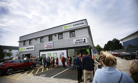 A queue of people stand outside the decorated new Oxfam Superstore, a grey warehouse looking building in Oxford