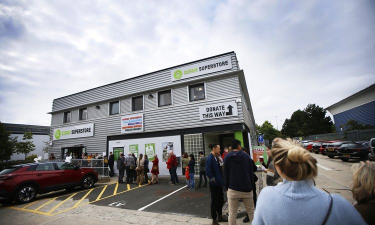 A queue of people stand outside the decorated new Oxfam Superstore, a grey warehouse looking building in Oxford