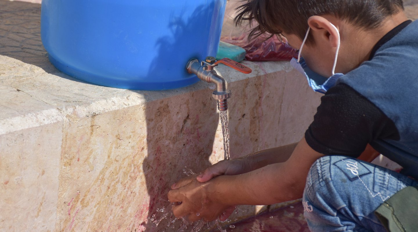 Am 8-year old boy wearing a facemask washes his hands in Syria