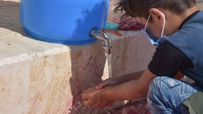 Am 8-year old boy wearing a facemask washes his hands in Syria