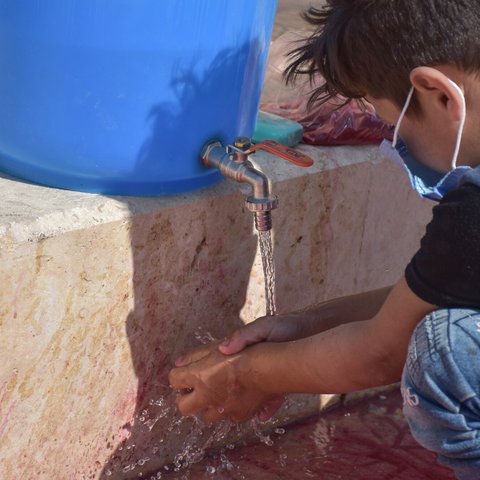 Am 8-year old boy wearing a facemask washes his hands in Syria