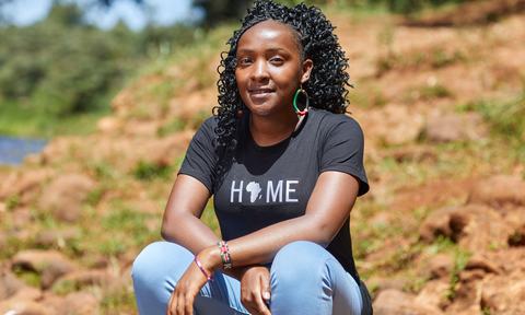 Elizabeth crouches down to pose outside smiling. She's wearing a T-shirt with Africa on it that says 'home' above it.