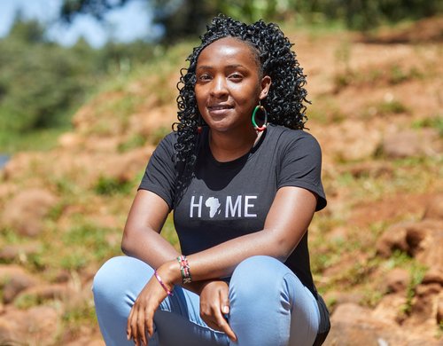 Elizabeth crouches down to pose outside smiling. She's wearing a T-shirt with Africa on it that says 'home' above it.