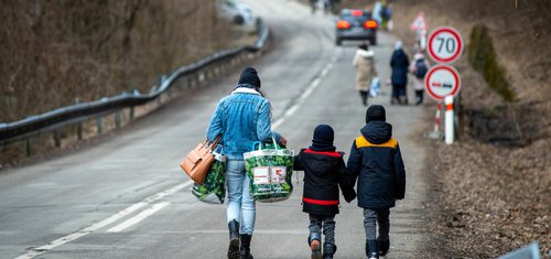 A woman with two children and carrying bags walk on a street to leave Ukraine after crossing the Slovak-Ukrainian border. Image: Peter Lazar/ AFP via Getty Images